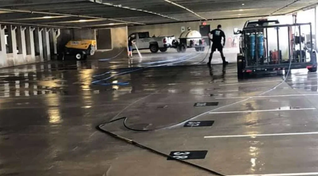 Commercial parking lot with dark oil stains being scrubbed and pressure washed clean for safer drives and better curb appeal.