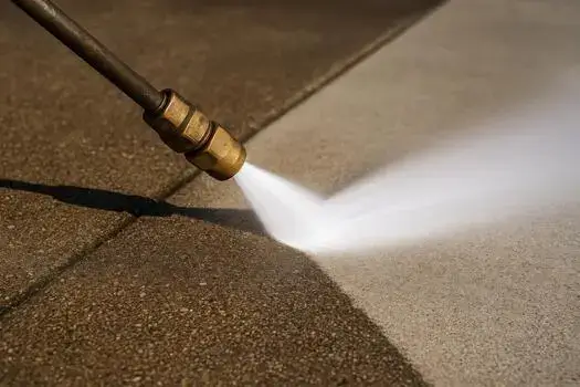 Pressure washer wand cutting a bright clean stripe through heavy gray grime on a durable outdoor concrete surface.